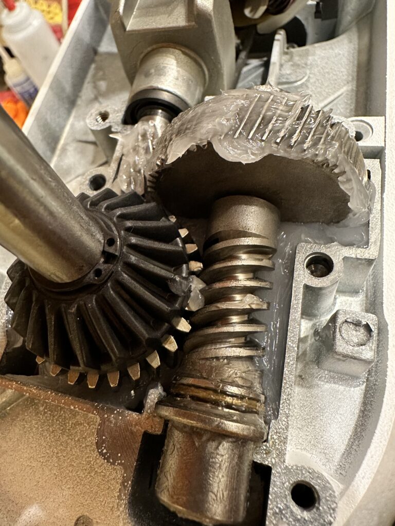 Photograph showing the exposed gear train of a KitchenAid "Professional 600" mixer, which design is shared with different model types.Visible are the main drive gear and "worm", with the beveled attachment drive gear visible on the left of center, and the "sacrificial" worm follower gear visible beneath that. Grease has been applied to the main drive gear and lower gear housing.